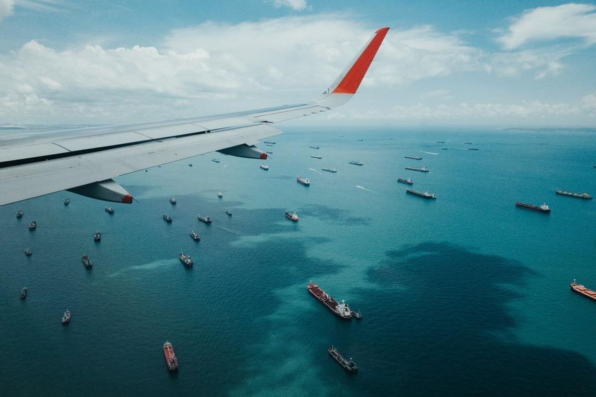 a plane wing flying over ships at sea